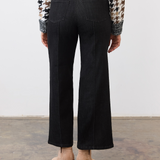 Person, shown from the back, wearing black ankle length jeans with a pin tuck down centre of the leg, with a black and tan houndstooth print sweater and tan ankle boots in a neutral studio backdrop.