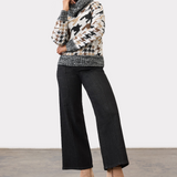 Person wearing black ankle length jeans with a pin tuck down centre of the leg, with a black and tan houndstooth print sweater and tan ankle boots in a neutral studio backdrop.
