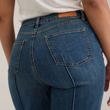Close up of a woman, from behind, modelling a white tank top with wide leg cropped jeans with a pintuck and unfinished hem with black high heels against  light backdrop.