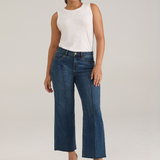 Woman modelling a white tank top with wide leg cropped jeans with a pintuck and unfinished hem with black high heels against  light backdrop.