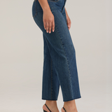 Woman modelling a white tank top with wide leg cropped jeans with a pintuck and unfinished hem with black high heels against  light backdrop.