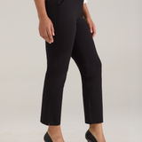 A model wearing black cropped ankle-length trousers with a white blouse and black pointed-toe high heels, shown from the waist down against a light gray studio background.