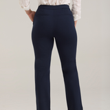 A woman, shown from the back, modeling a white textured button-up blouse and navy cropped trousers with tan pointed-toe heels, standing against a light gray studio background.