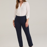 A woman modeling a white textured button-up blouse and navy cropped trousers with tan pointed-toe heels, standing against a light gray studio background.