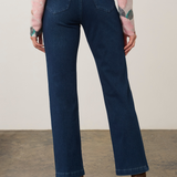 A model shown from the back wearing dark blue straight-leg jeans, a pink floral long-sleeve top, and brown suede ankle boots, standing against a neutral studio background.