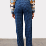 Person, shown from the back, wearing a tone on tone blue houndstooth straight leg jean, with a pintuck, with a diamond print sweater and brown boots on a neutral background.