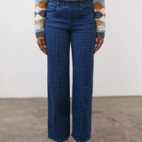 Person wearing a tone on tone blue houndstooth pull on straight leg jean, with a centre pintuck, with a diamond print sweater and tan boots on a neutral background.