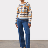 Person wearing a tone on tone blue houndstooth straight leg jean, with a centre pintuck, with a diamond print sweater and tan boots on a neutral background.