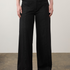 A model from the waist down wearing black wide-leg denim pants, a black top, and black shoes, standing against a neutral studio background.