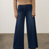 A model wearing dark blue wide-leg denim jeans, a beige textured knit sweater, and beige pointed-toe heels, standing against a neutral studio backdrop.