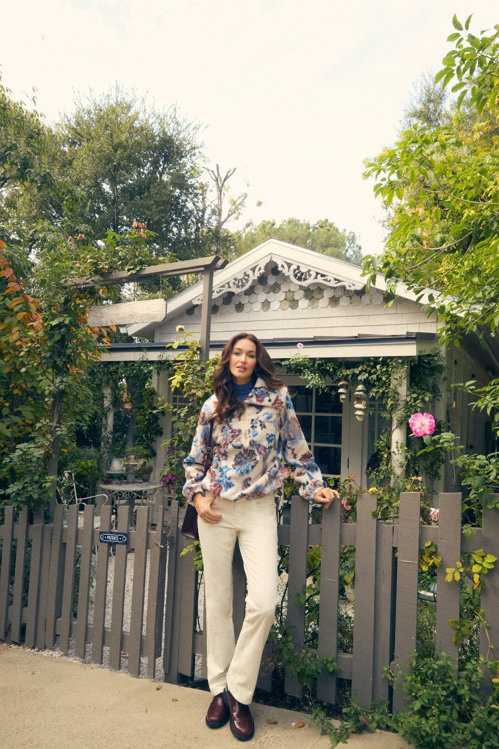 Woman standing in front of a wooden gate with greenery