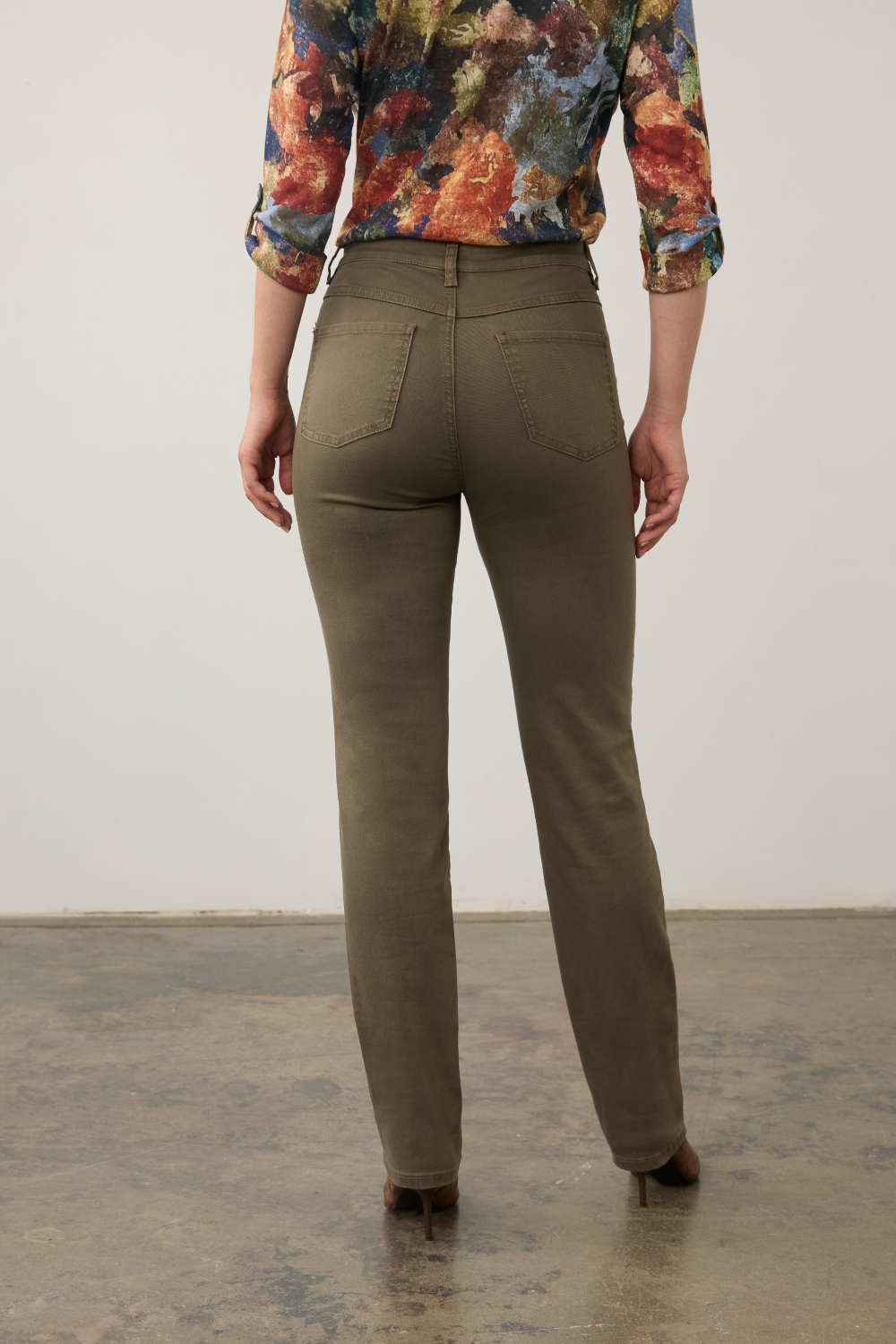 Woman, shown from the back, modelling a multi coloured shirt with green jeans  and brown boots photographed against a light background.