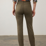 Woman, shown from the back, modelling a multi coloured shirt with green jeans  and brown boots photographed against a light background.