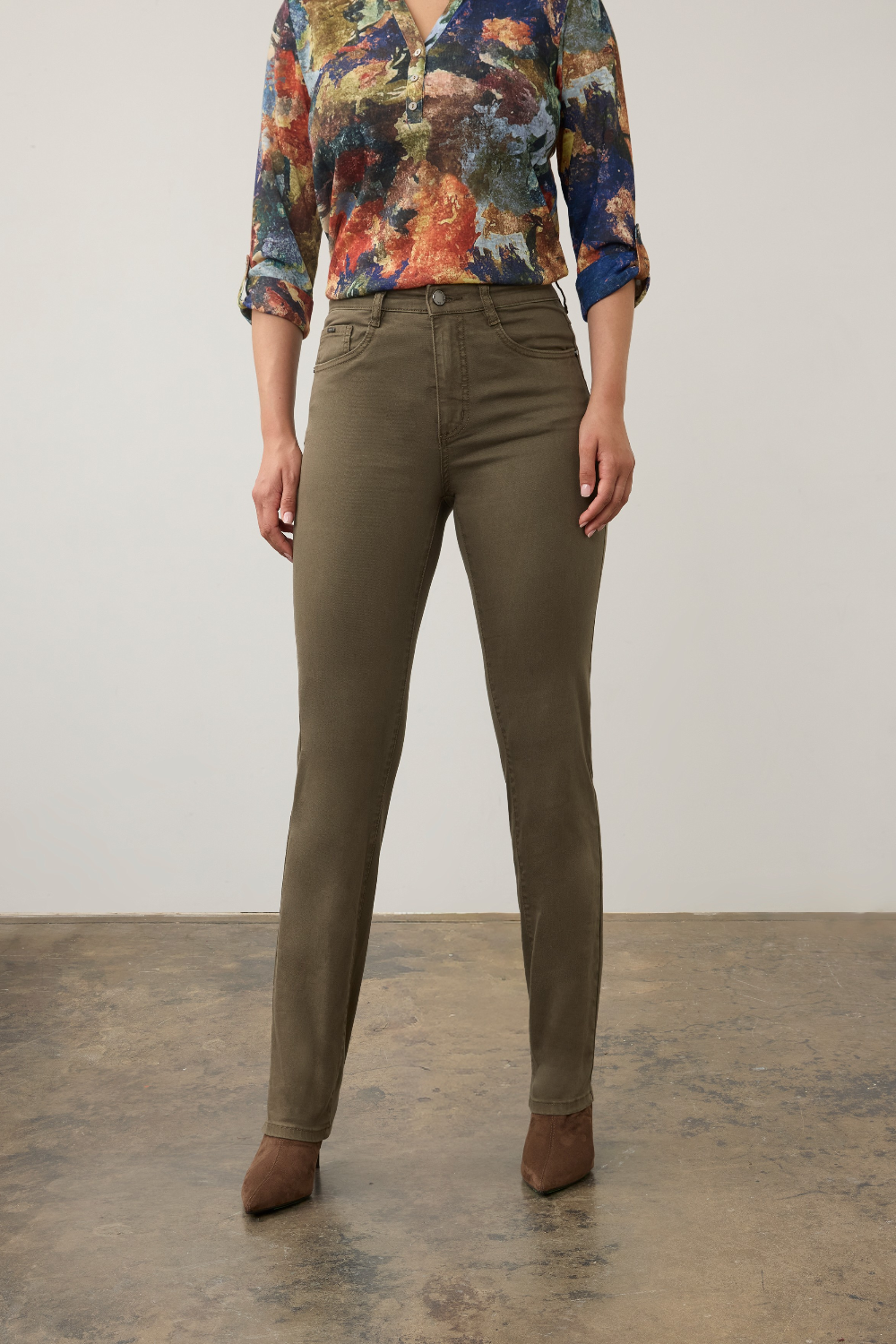 Woman modelling a multi coloured shirt with green jeans  and brown boots photographed against a light background.