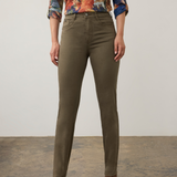 Woman modelling a multi coloured shirt with green jeans  and brown boots photographed against a light background.