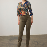 Woman modelling a multi coloured shirt with green jeans  and brown boots photographed against a light background.