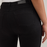 Rear view of a model wearing black high-waisted  jeans and a white top, against a light gray studio background.