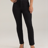 A woman modeling a pair of black jeans with a white sleeveless top and black high heels, standing against a light gray studio background.