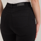 Rear view of a model wearing black high-waisted  jeans and a white top, against a light gray studio background.