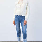 Woman wearing a white puffer vest, cream turtleneck, blue jeans, and white shoes on a plain background