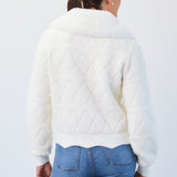 Person wearing a white quilted jacket and blue jeans on a light gray background