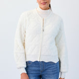Woman wearing a white zip-up sweater over a turtleneck with blue jeans on a light gray background