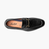 Black loafer shoe with gold buckle on a white background