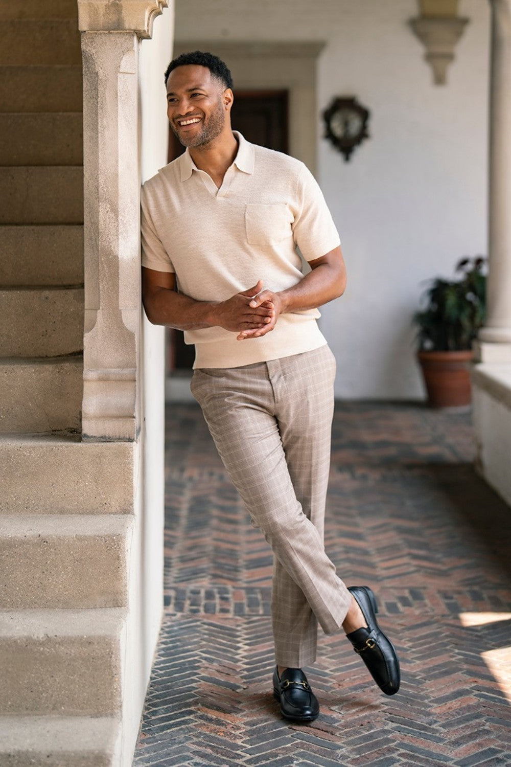 Man standing on a staircase wearing a beige shirt and light-colored pants.