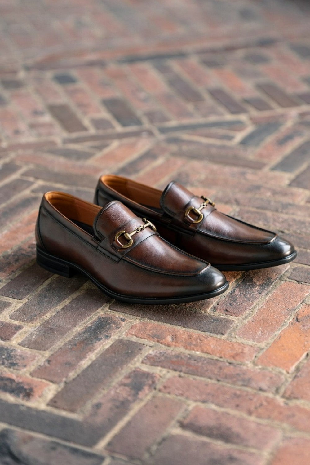 Pair of brown loafers with gold buckles on a brick floor