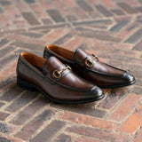 Pair of brown loafers with gold buckles on a brick floor