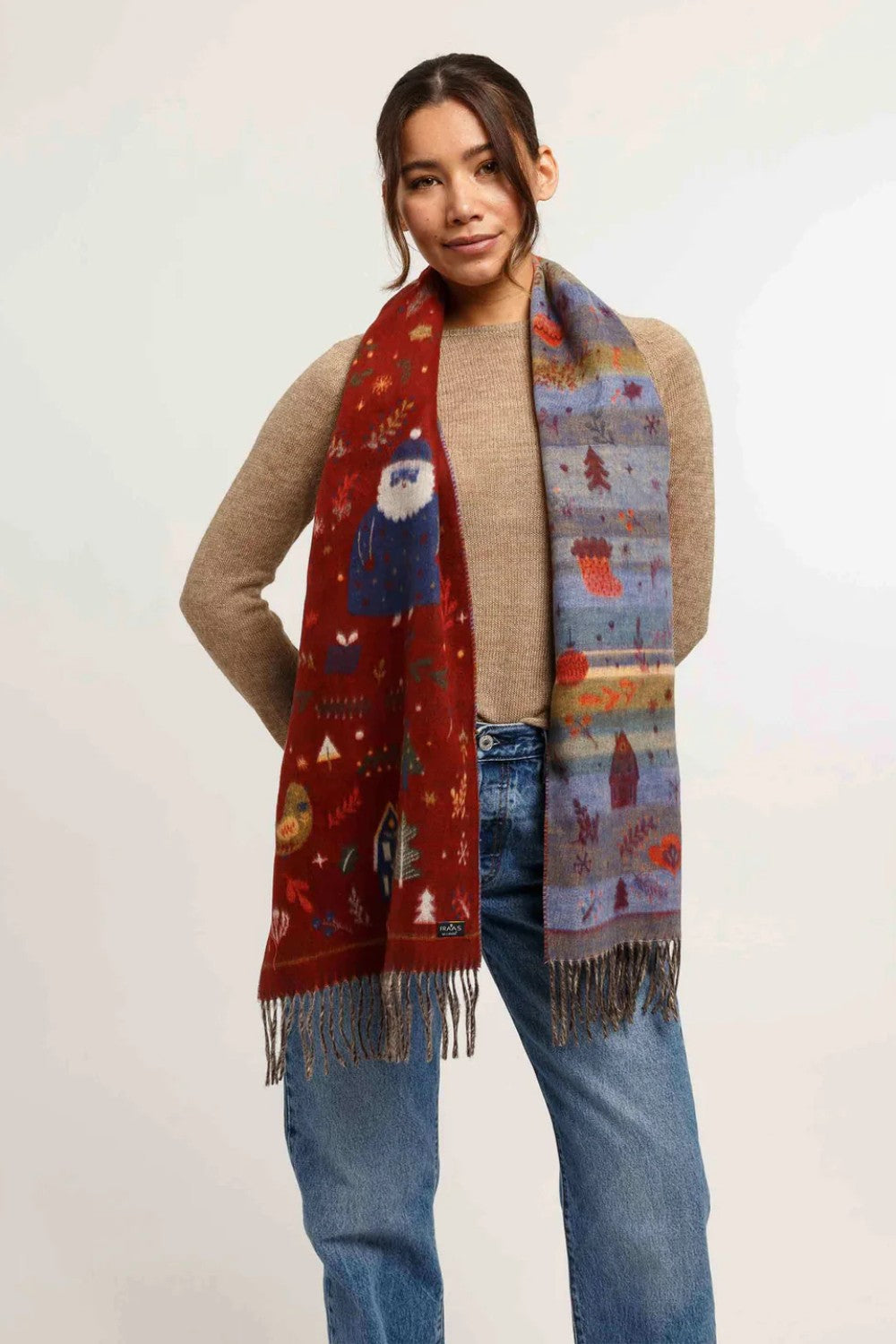 Woman wearing Christmas themed scarf with beige sweater and blue jeans on light background