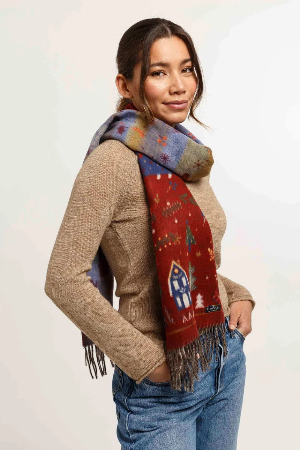 Woman wearing Christmas themed scarf with beige sweater and blue jeans on light background