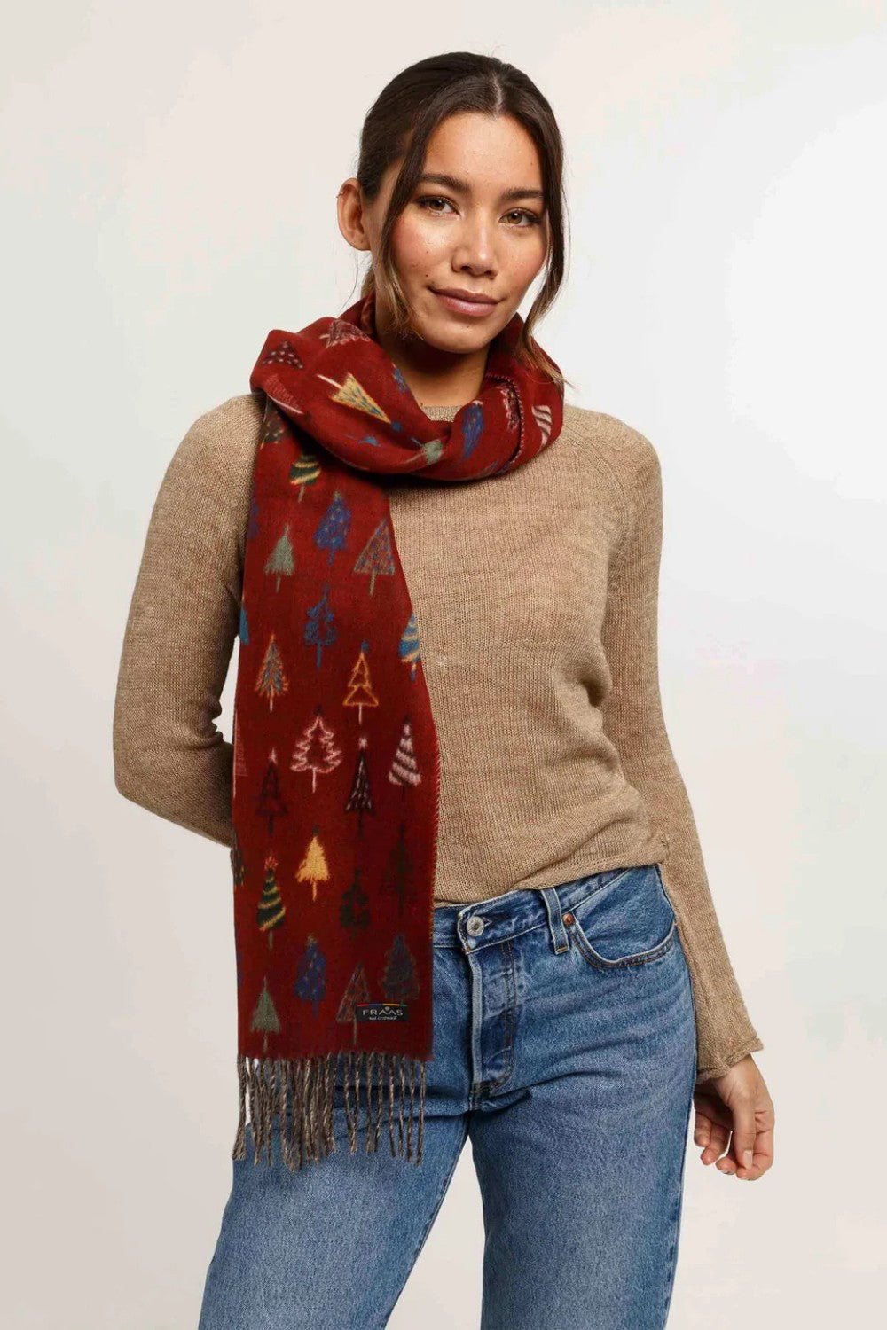 Woman wearing a patterned red scarf, beige sweater, and blue jeans on a white background