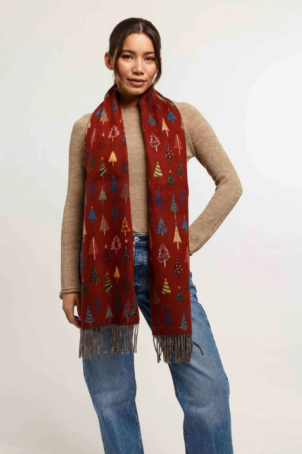 Woman wearing a red patterned scarf with fringes on a plain background