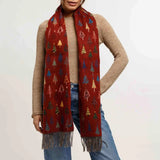 Woman wearing a red patterned scarf with fringes on a plain background