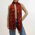 Woman wearing a red patterned scarf with fringes on a plain background
