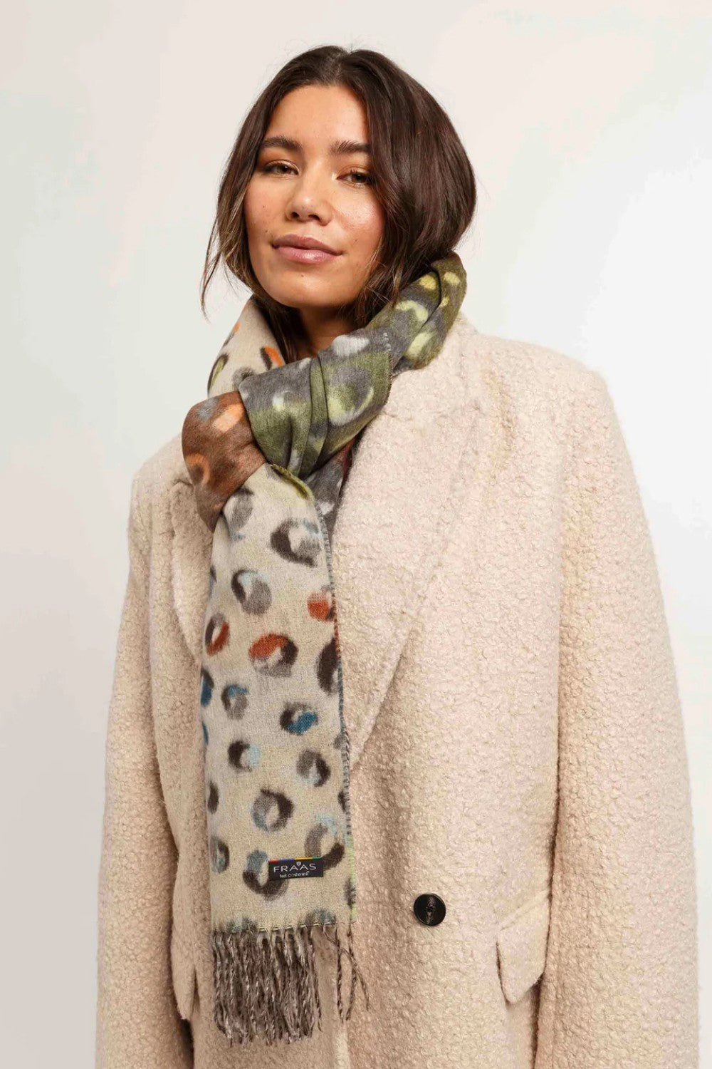 Woman wearing a patterned scarf and beige coat against a plain background