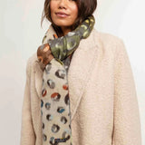 Woman wearing a patterned scarf and beige coat against a plain background