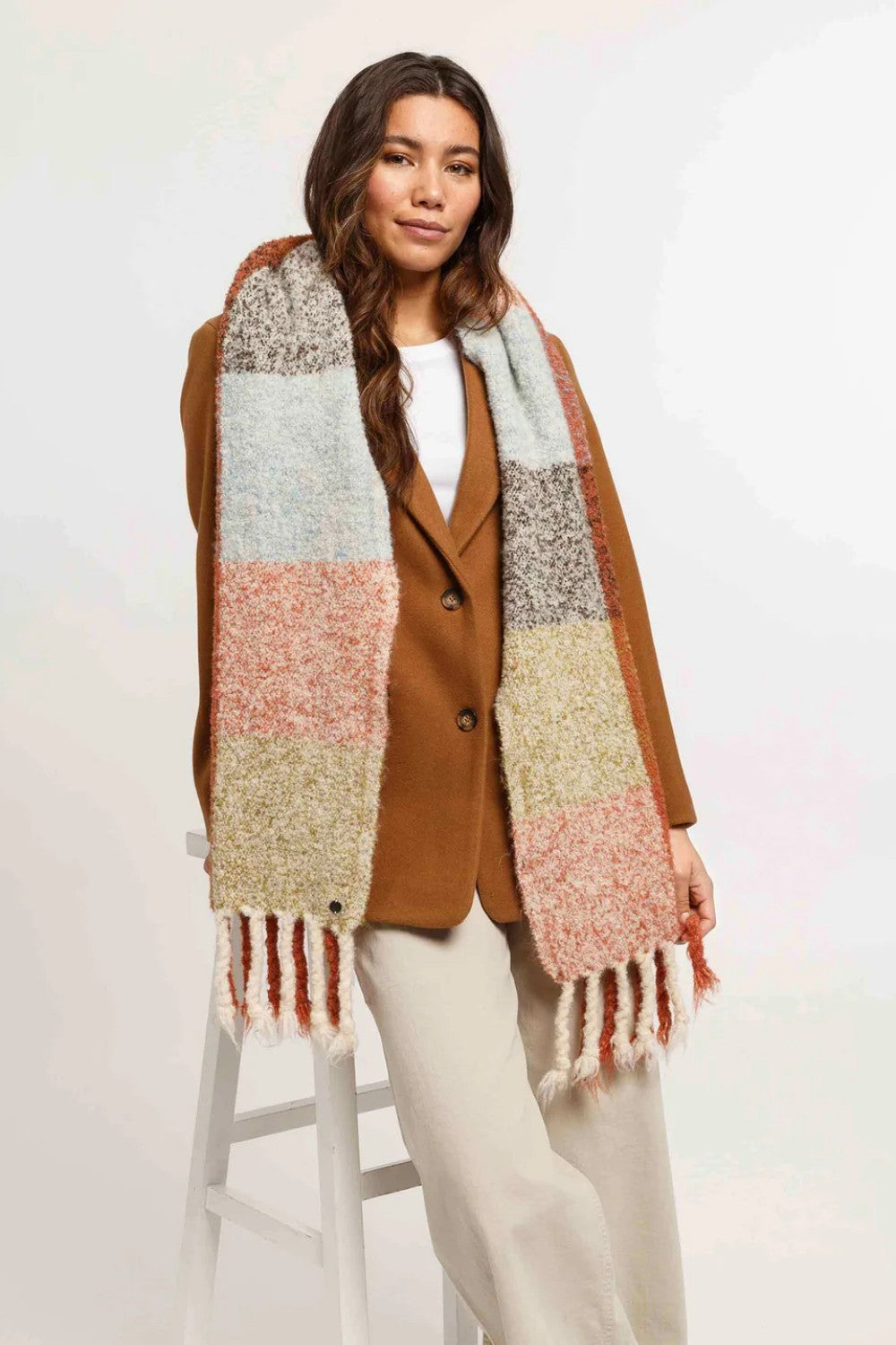 Woman wearing a colorful scarf and brown coat on a white background