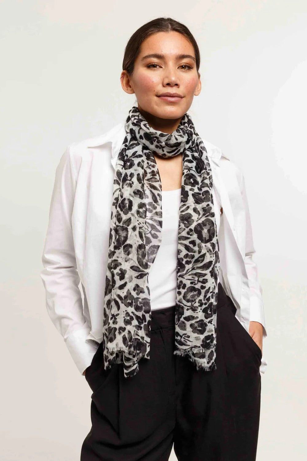 Woman wearing a white shirt, black pants, and a patterned scarf against a plain background