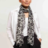 Woman wearing a white shirt, black pants, and a patterned scarf against a plain background