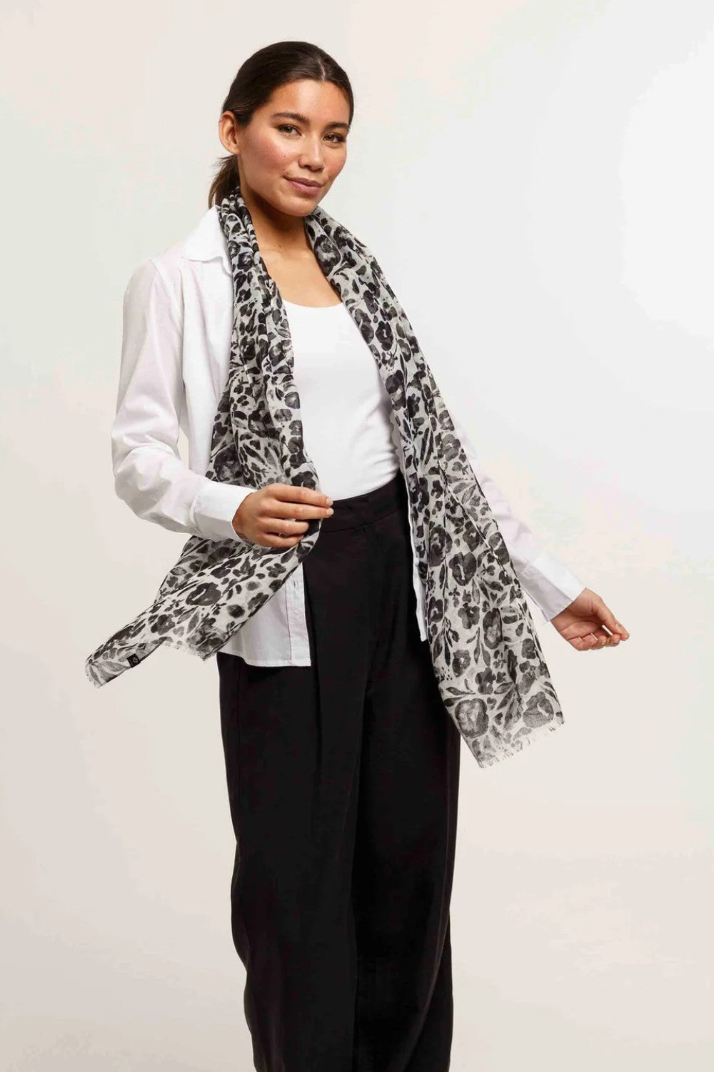 Woman wearing a white blouse, black pants, and a patterned scarf against a plain background