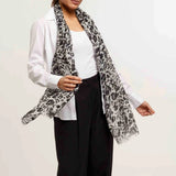 Woman wearing a white blouse, black pants, and a patterned scarf against a plain background