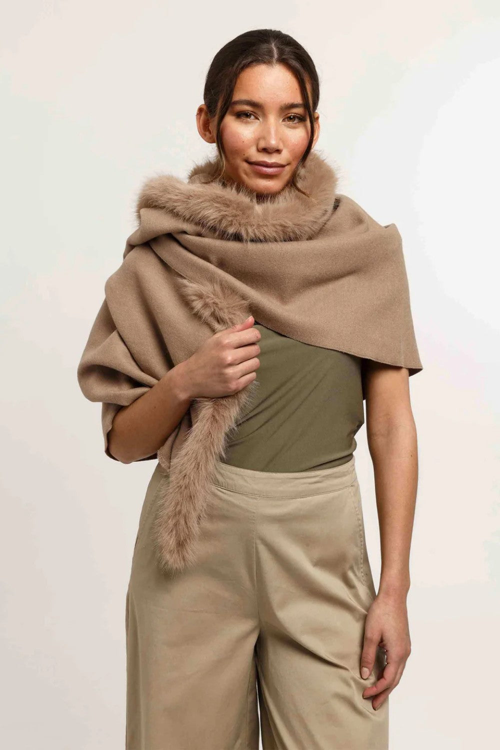 Woman wearing a beige shawl with fur trim on a plain background