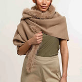 Woman wearing a beige shawl with fur trim on a plain background