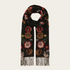 A black scarf with a detailed floral pattern in red, orange, and green, finished with fringe on both ends, displayed against a light off-white background.