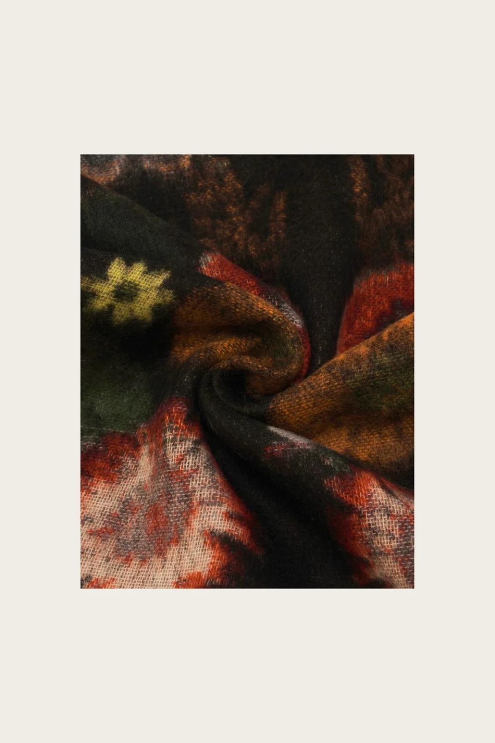 A close-up of a textured knit fabric with a pattern in black, rust red, olive green, and cream, arranged in a central square on a light beige background.