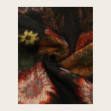A close-up of a textured knit fabric with a pattern in black, rust red, olive green, and cream, arranged in a central square on a light beige background.