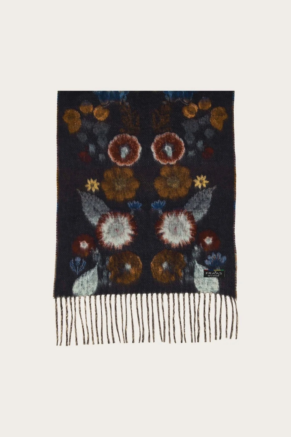 A rectangular dark navy knit scarf with a floral pattern in rust, brown, cream, and blue, finished with fringe at the bottom, shown on a light beige background.