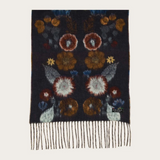 A rectangular dark navy knit scarf with a floral pattern in rust, brown, cream, and blue, finished with fringe at the bottom, shown on a light beige background.